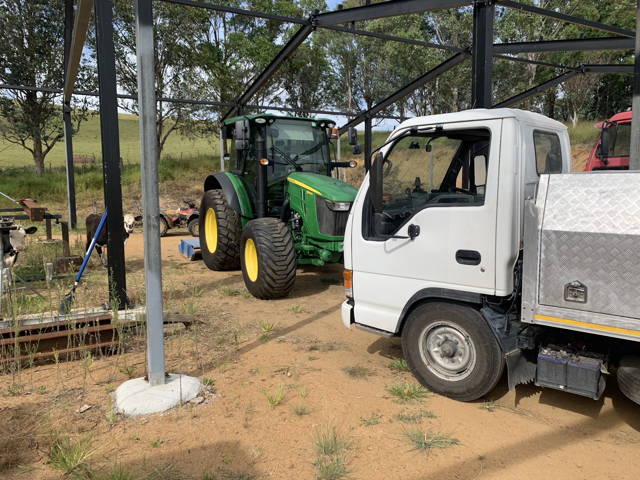 The service truck and a John Deere tractor at a farm shed, with cattle in the yard alongside