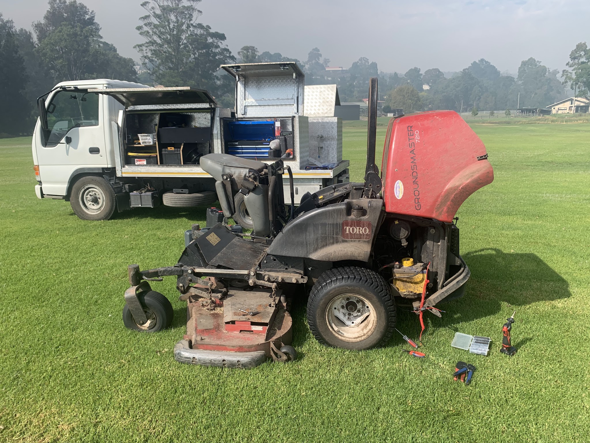 A Toro Groundsmaster ride on mower opened up on turf, with the service truck and its tool drawers behind it