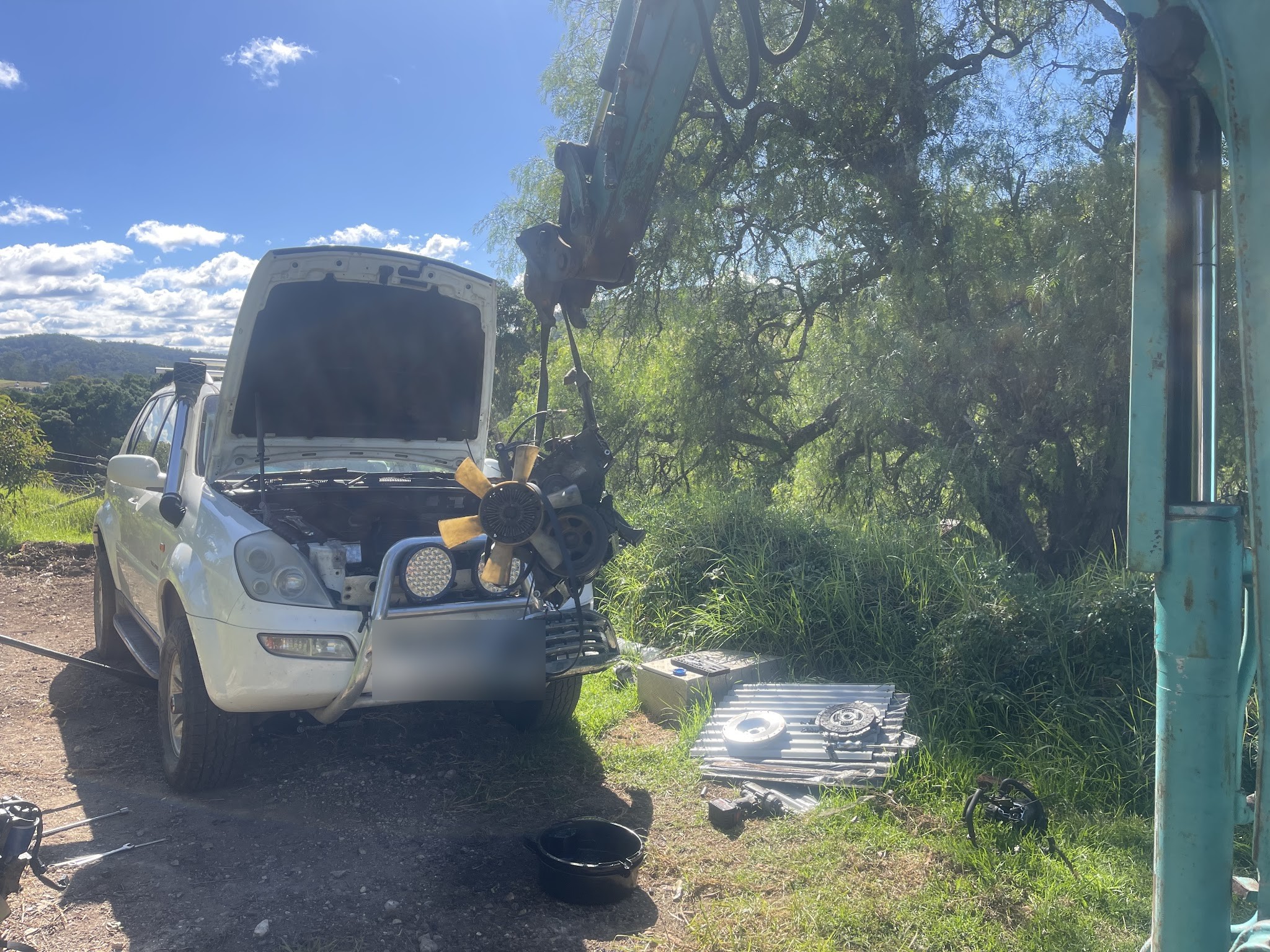 A four wheel drive with its engine lifted out on a crane on a rural block